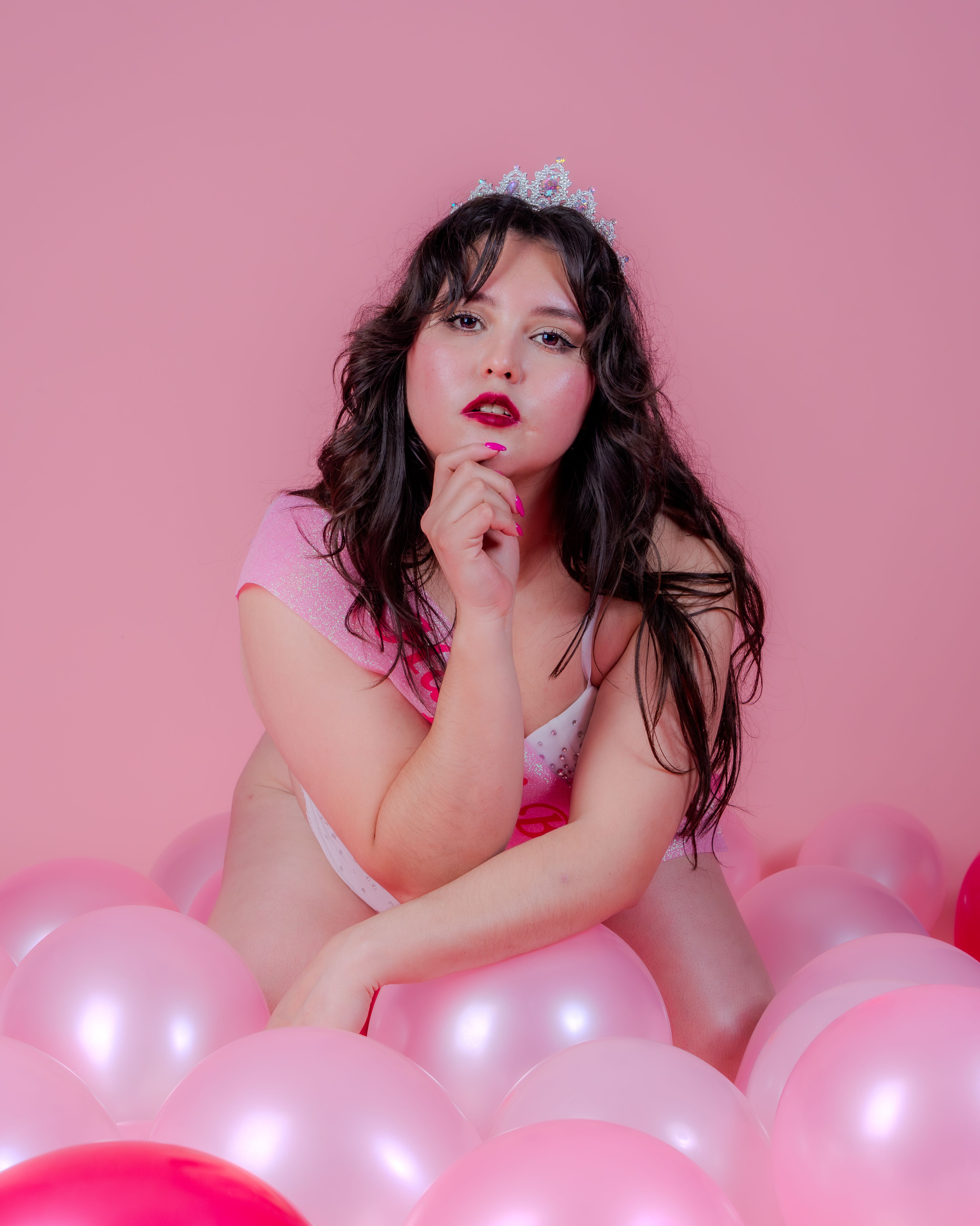Confident young woman in pink surrounded by balloons, embodying elegance and joy.