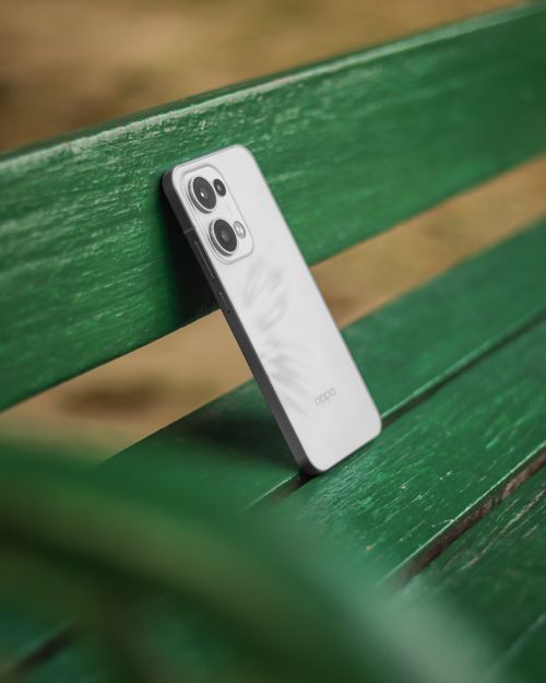 Free A white smartphone leaning against a green wooden bench in an outdoor park setting. Stock Photo