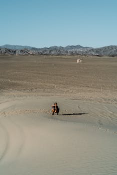 一个人坐在荒芜的沙漠中，远处群山起伏，天空湛蓝