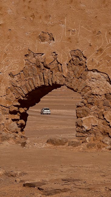 A serene view of a white car through a stone archway in the Iranian desert.