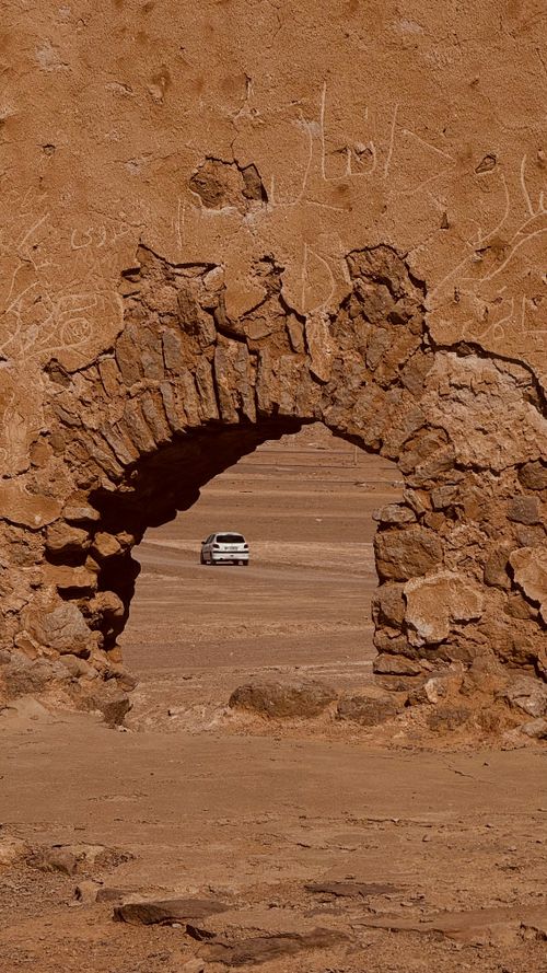 Free A serene view of a white car through a stone archway in the Iranian desert. Stock Photo