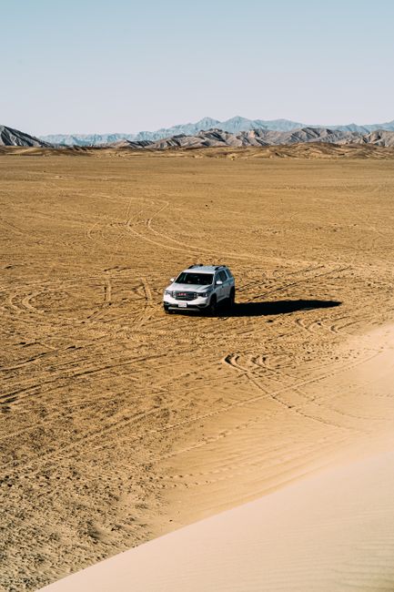 A white SUV navigates the expansive desert terrain under clear blue skies, showcasing adventure and exploration.