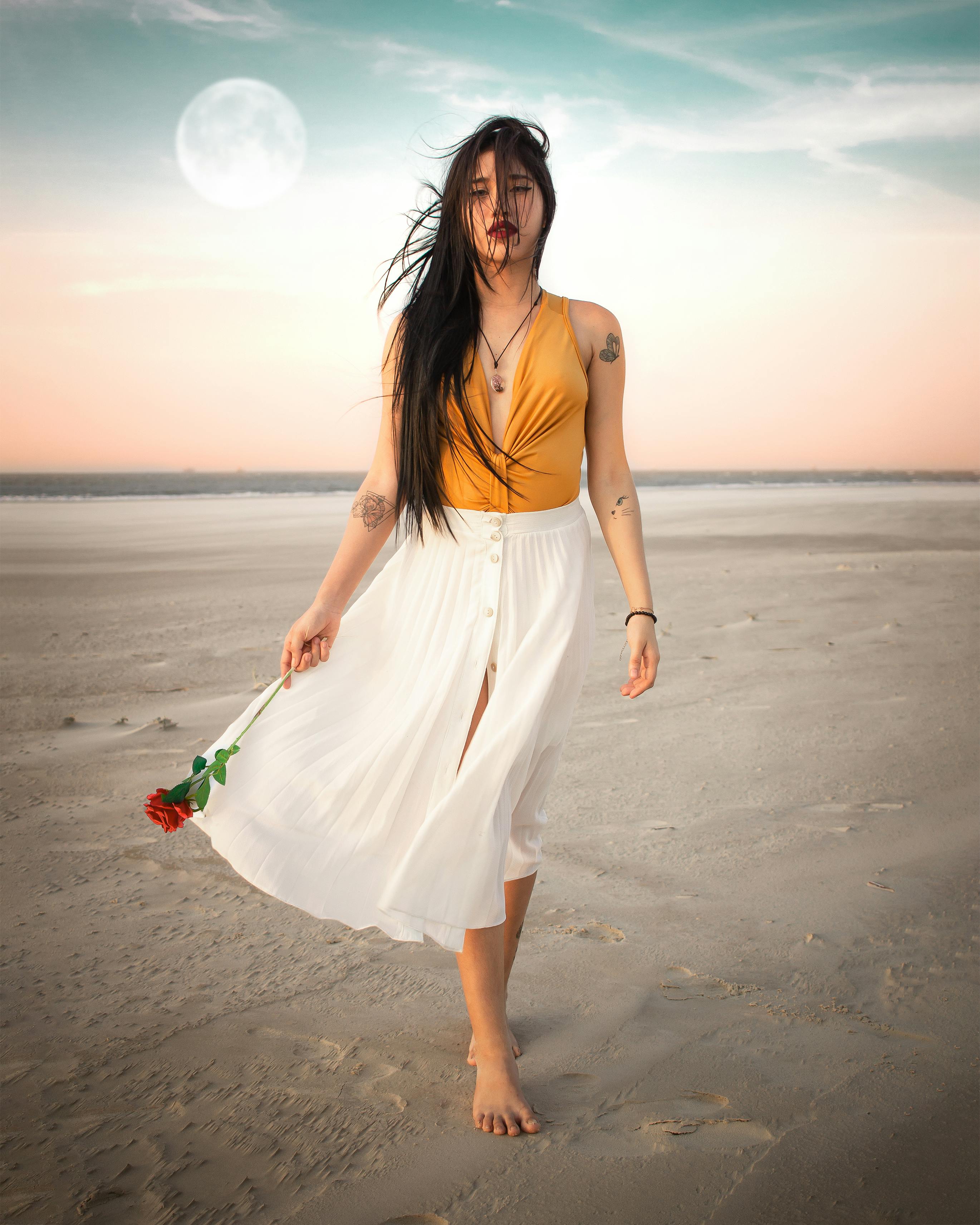 一位长发优雅的女人，在满月下的沙滩上捧着一朵玫瑰