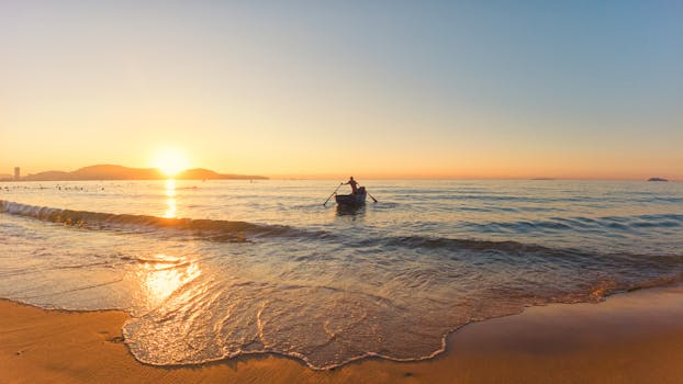 A serene scene of a lone fisherman rowing at sunrise on Quy Nhơn beach, Bình Định, Vietnam.