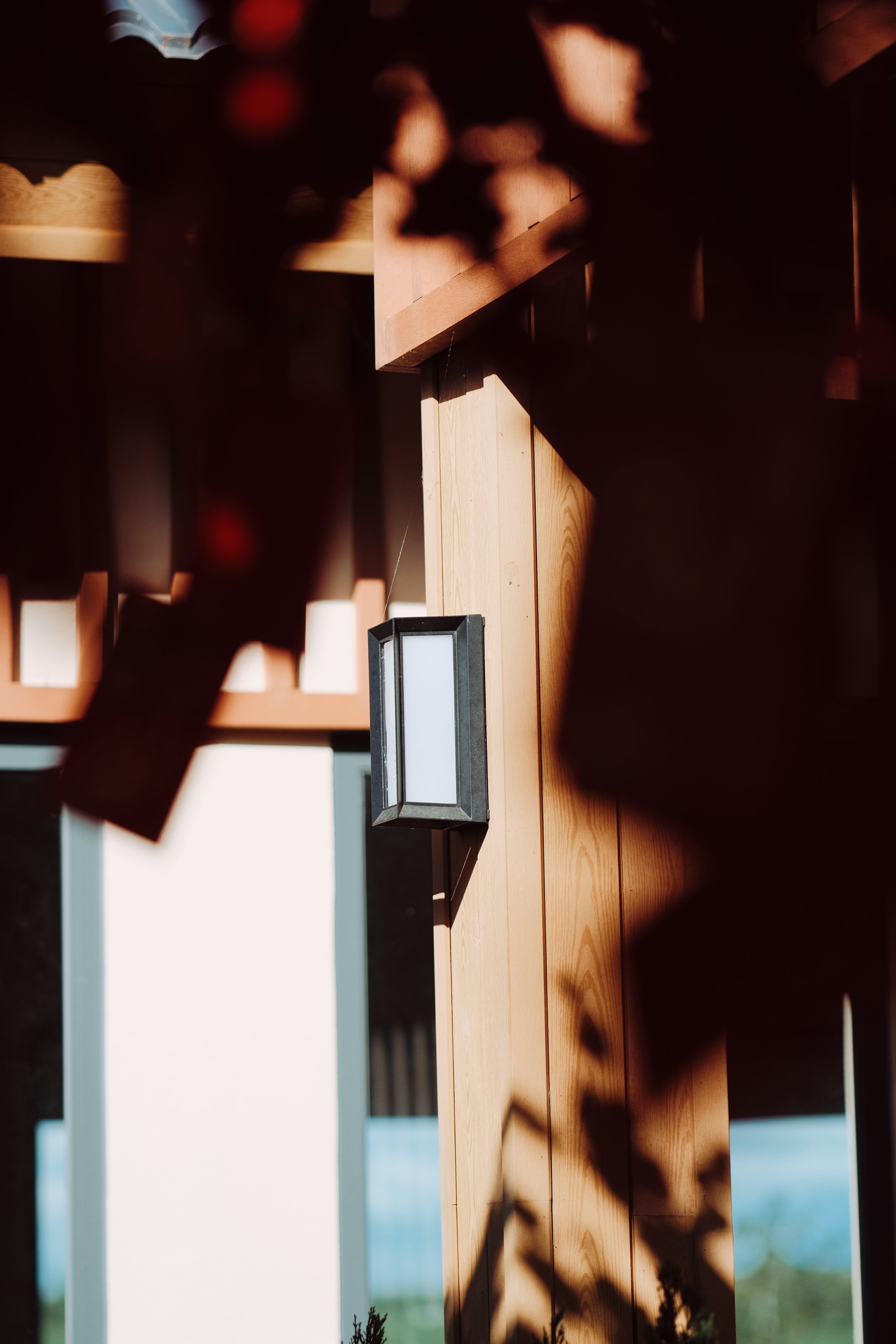 Free A close-up of a wooden building exterior with a modern lamp, highlighted by sunlit shadows. Stock Photo