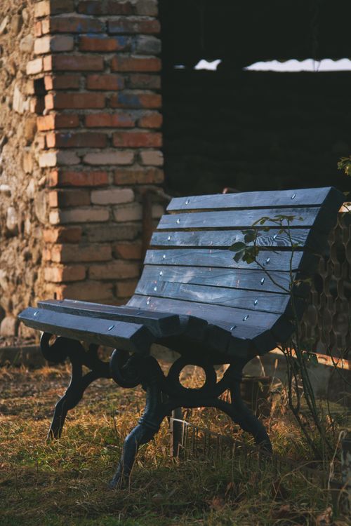 Free A rustic wooden bench in a sunlit outdoor space with brick and stone background. Stock Photo