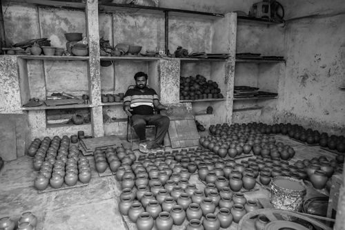 Free Black and white photo of a potter sitting in a workshop filled with clay pots in Hyderabad, India. Stock Photo