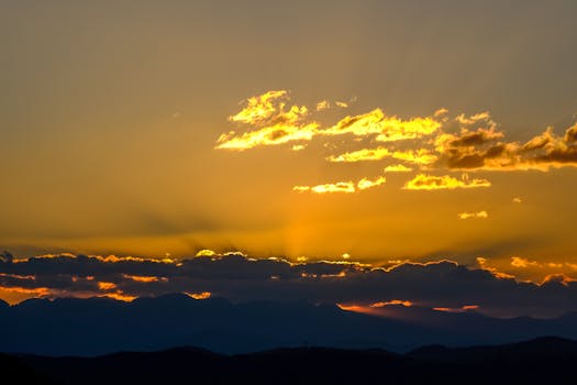 Stunning golden sunset with clouds over a silhouetted mountain range, creating a warm and serene atmosphere.