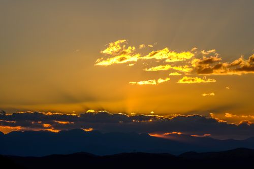 Free Stunning golden sunset with clouds over a silhouetted mountain range, creating a warm and serene atmosphere. Stock Photo