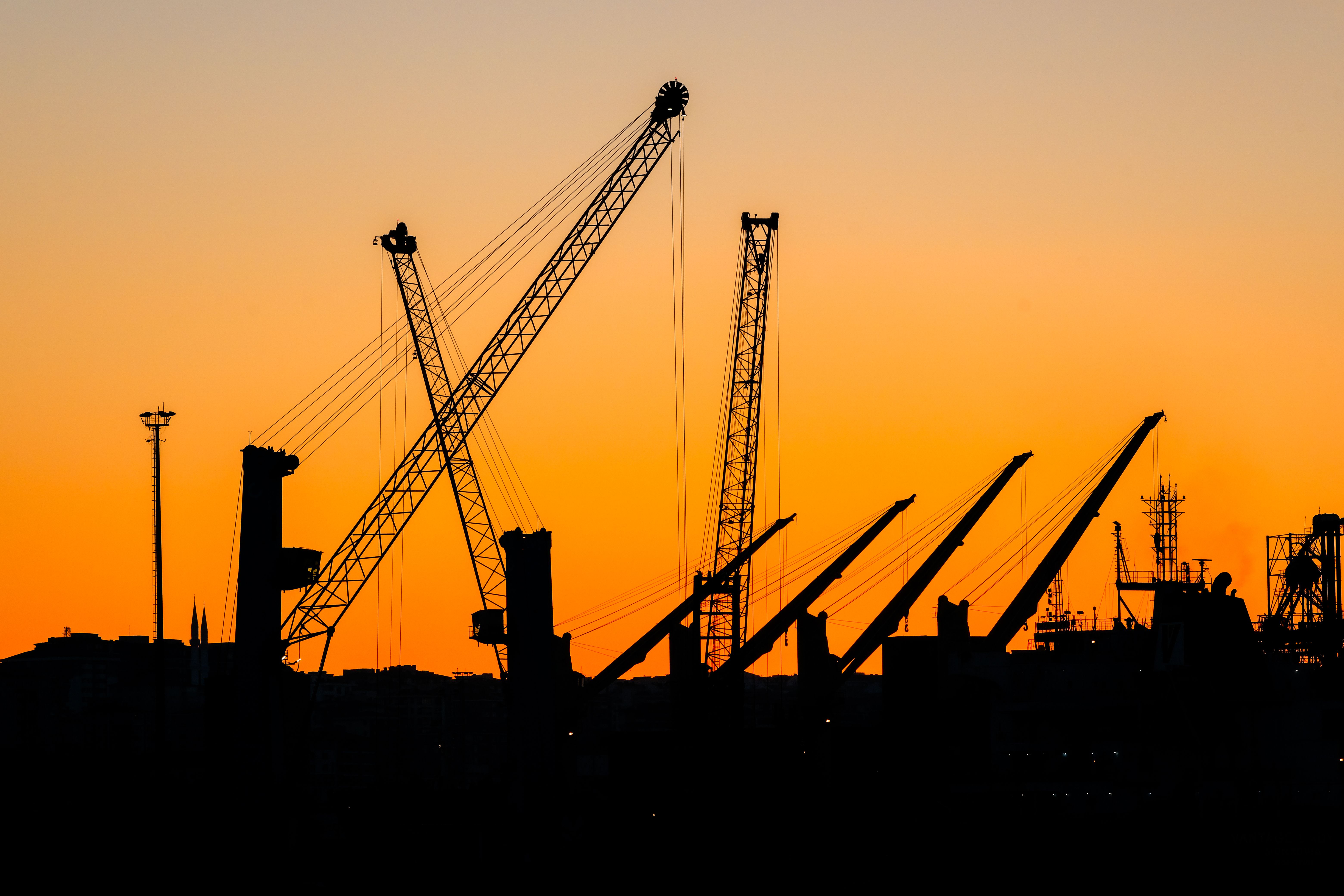 Gratis Silhuet af industrielle kraner mod en pulserende solnedgangsskyline. Ideel til urbane og industrielle temaer. Lagerfoto
