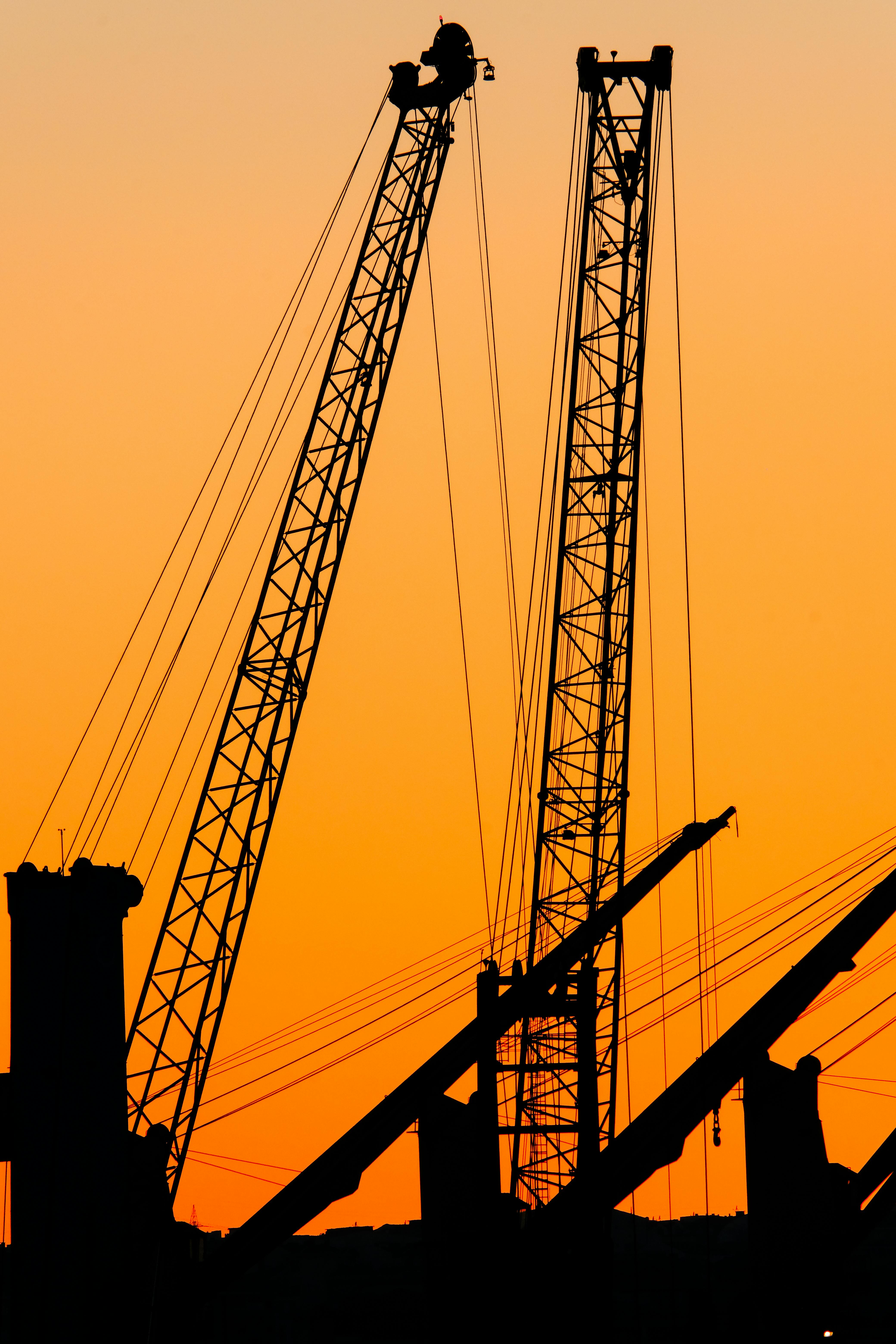 Silhouetted cranes against an orange sunset sky, showcasing construction and industry.