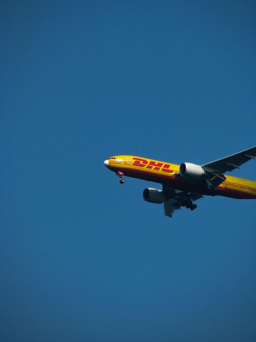 Free A DHL cargo plane flying against a clear blue sky during the day. Ideal for aviation and logistics themes. Stock Photo