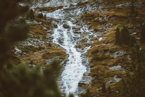 Free Beautiful waterfall cascading down rocky mountain amidst lush green forest. Stock Photo