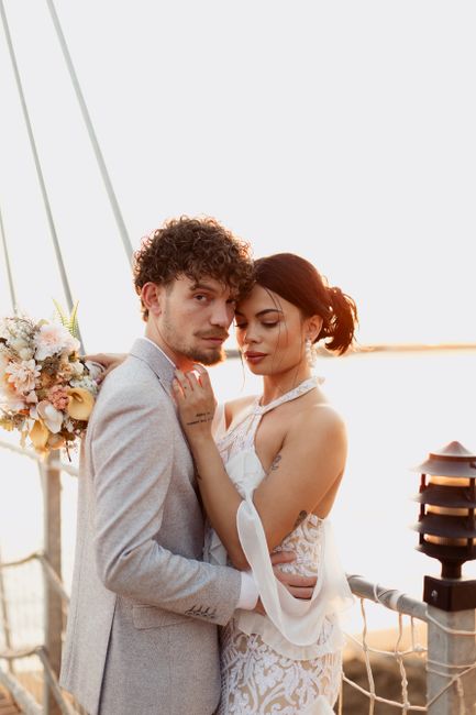 Romantic wedding couple embracing at sunset on a pier with a bouquet.