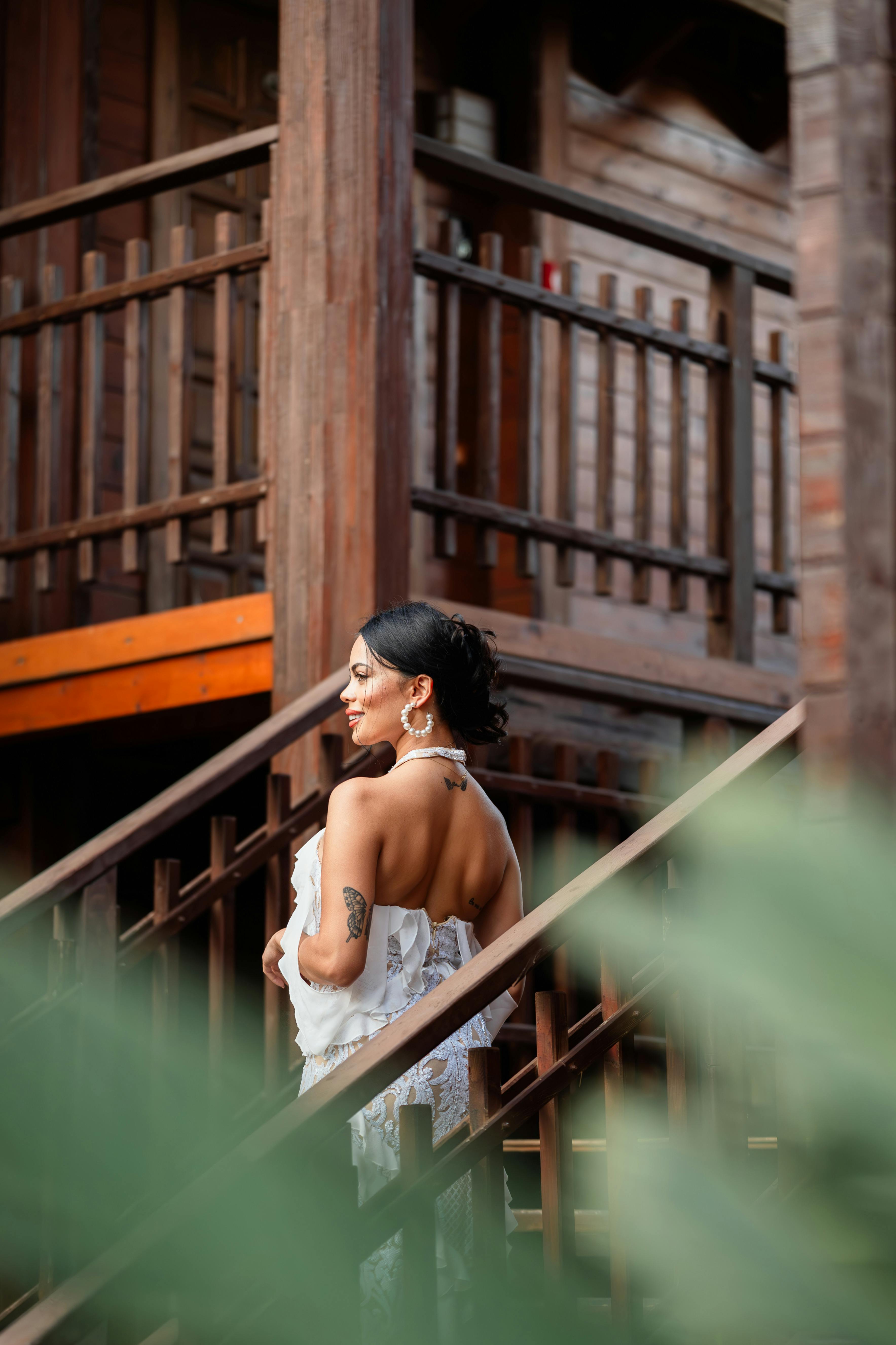 Woman in elegant attire posing on rustic wooden stairs, bringing a serene and stylish feel to the outdoors.