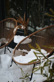 Wicker patio chairs blanketed with fresh snow on a serene winter day.
