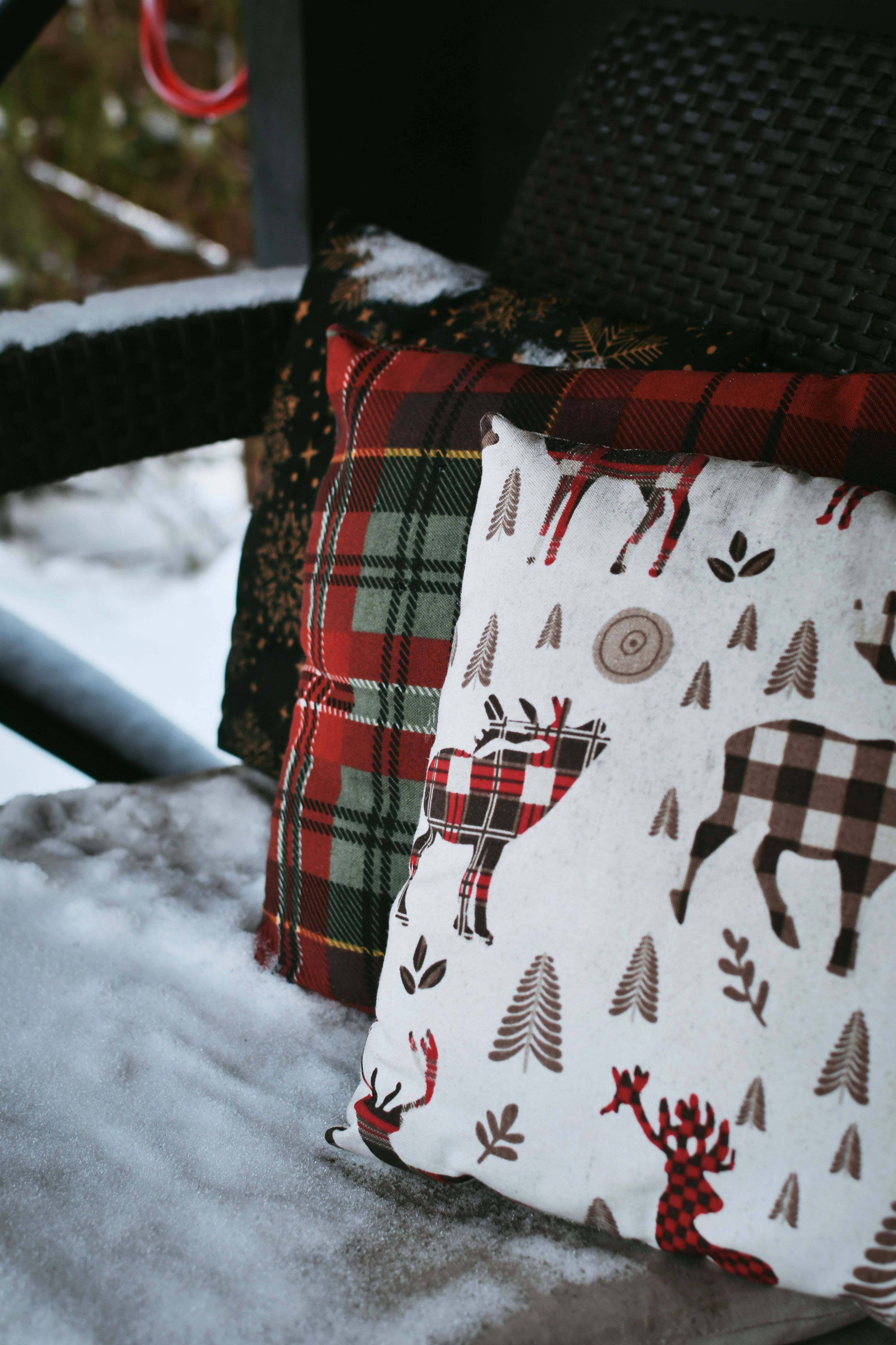 Cozy plaid and reindeer cushions on a snowy porch, perfect for winter holidays.