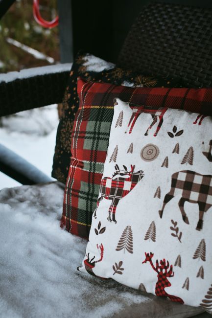 Cozy plaid and reindeer cushions on a snowy porch, perfect for winter holidays.