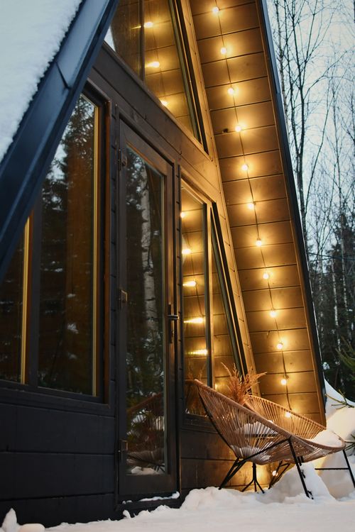 Free A-frame cabin with strings of lights creating a cozy winter ambiance in the snow. Stock Photo