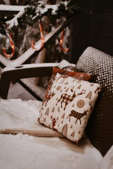 Snow-covered patio with festive cushion and holiday decor creates a warm winter scene.