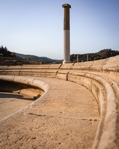 Free Explore the ancient stone amphitheater with its iconic lone column in a sunny outdoor setting. Stock Photo