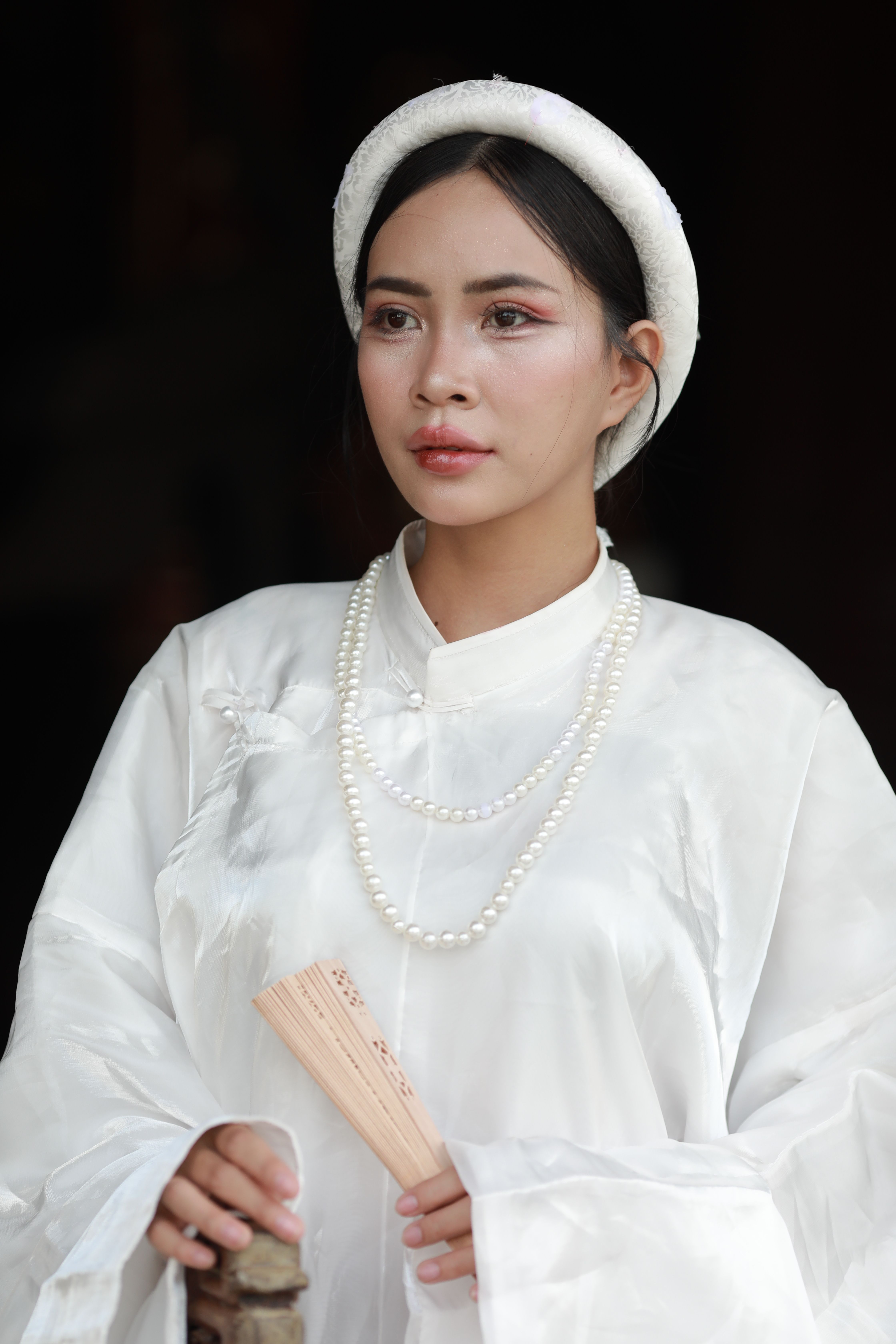 Portrait of elegant woman in traditional white outfit holding a fan with grace.