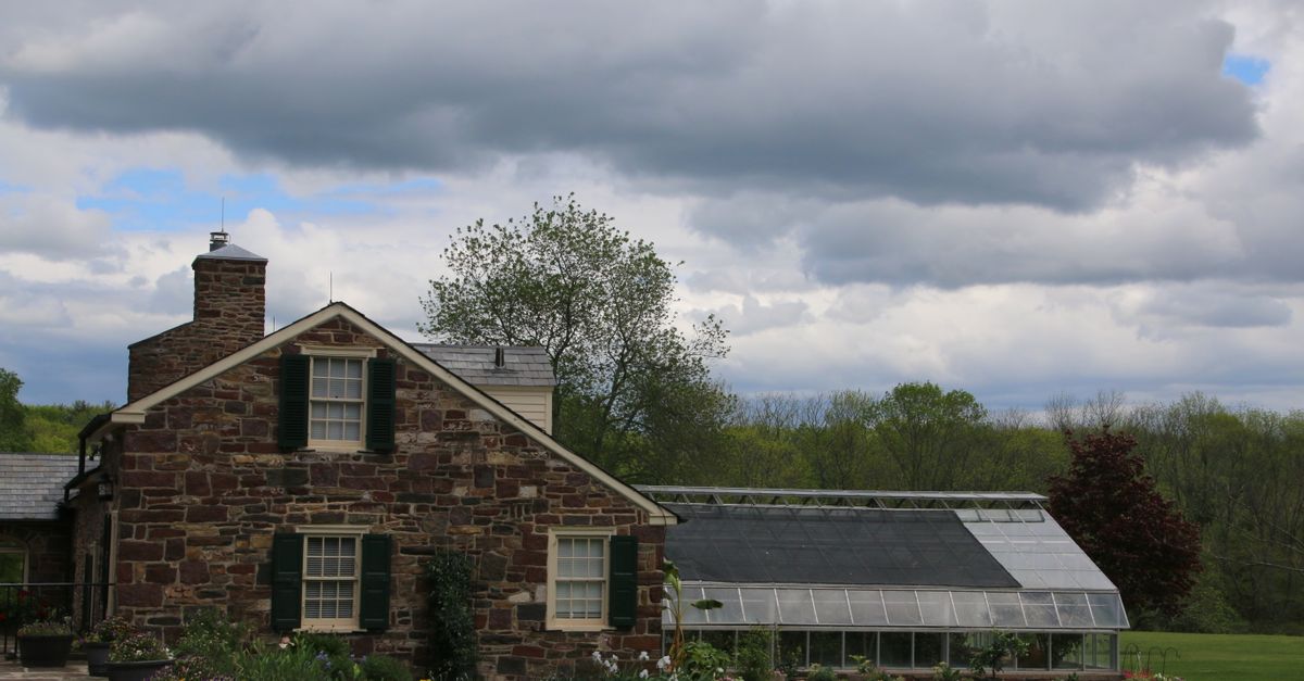 Beautiful historic stone house with attached greenhouse, surrounded by lush greenery in Dublin, Pennsylvania.