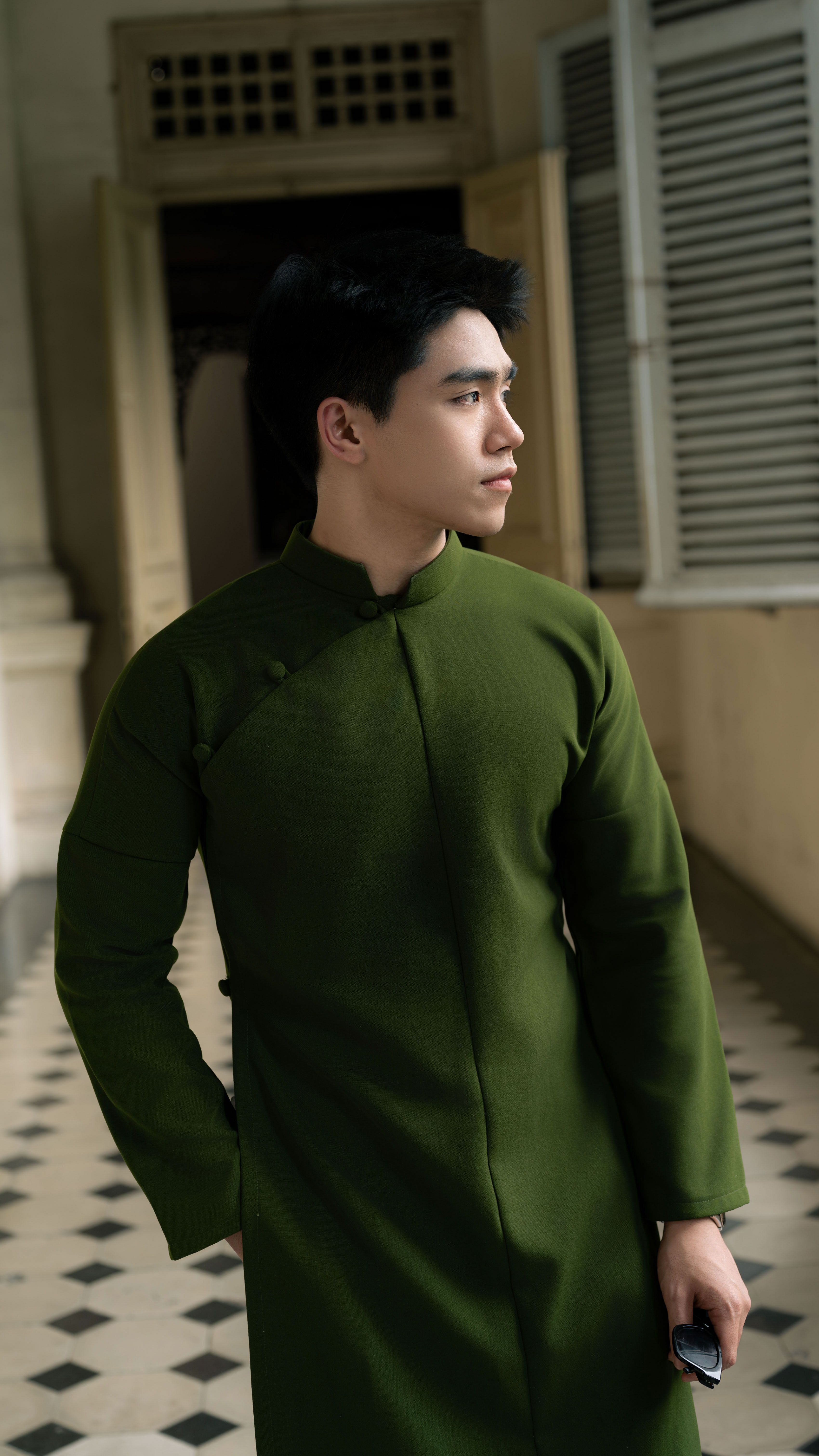 Man in a long green traditional dress standing in a hallway looking sideways