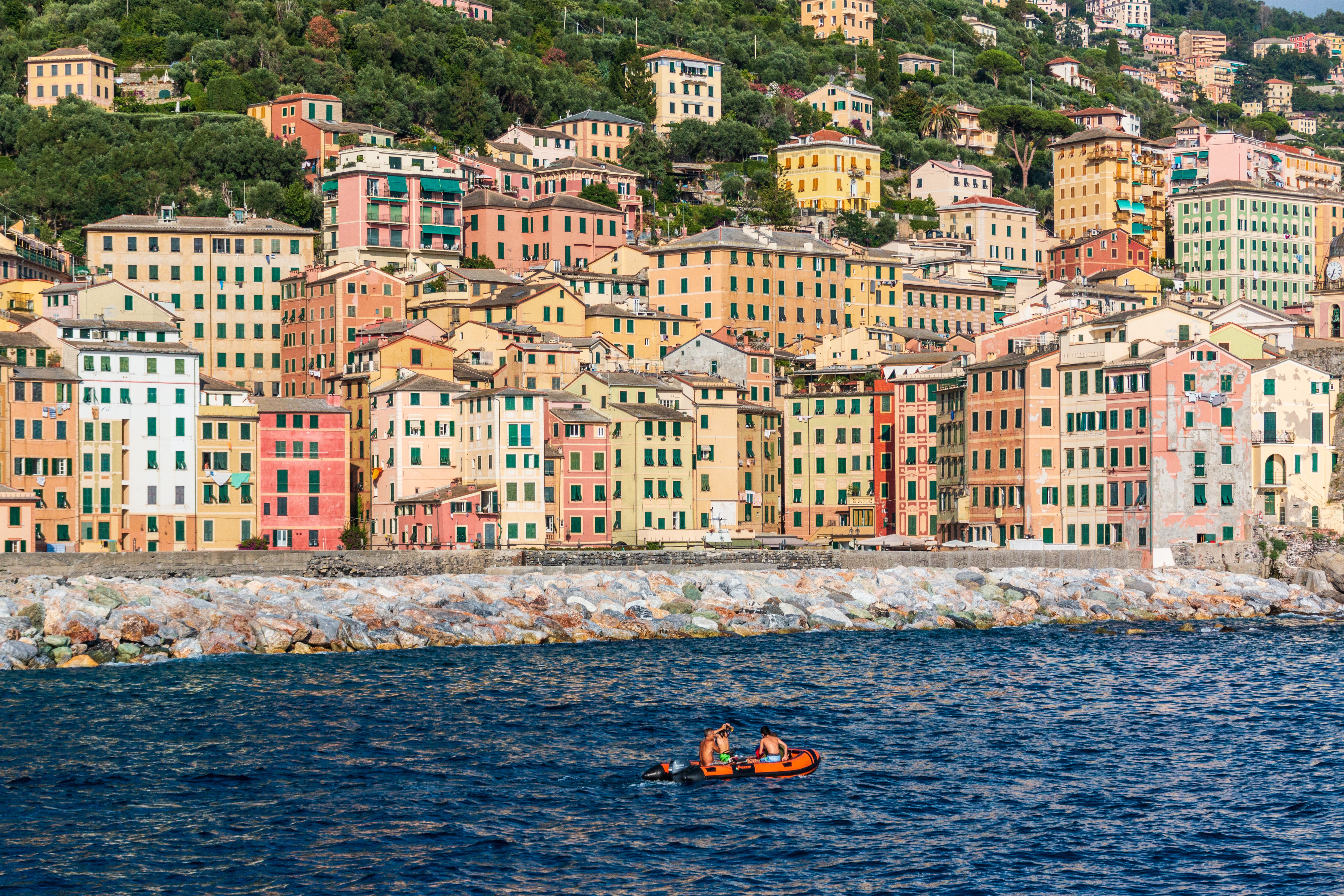 Lively scene of colorful buildings by the sea in Camogli, Liguria, with people rowing.