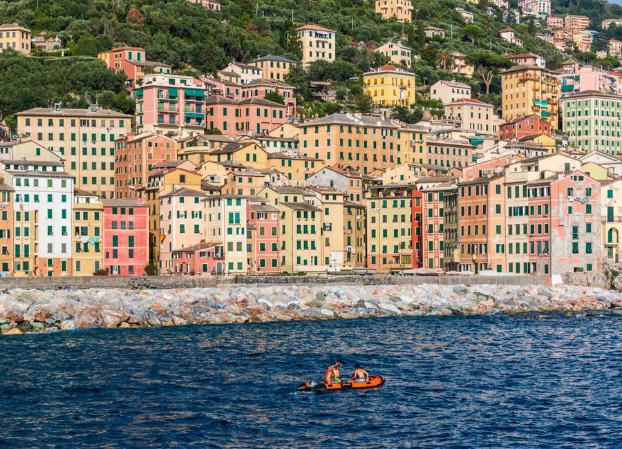 Lively scene of colorful buildings by the sea in Camogli, Liguria, with people rowing.