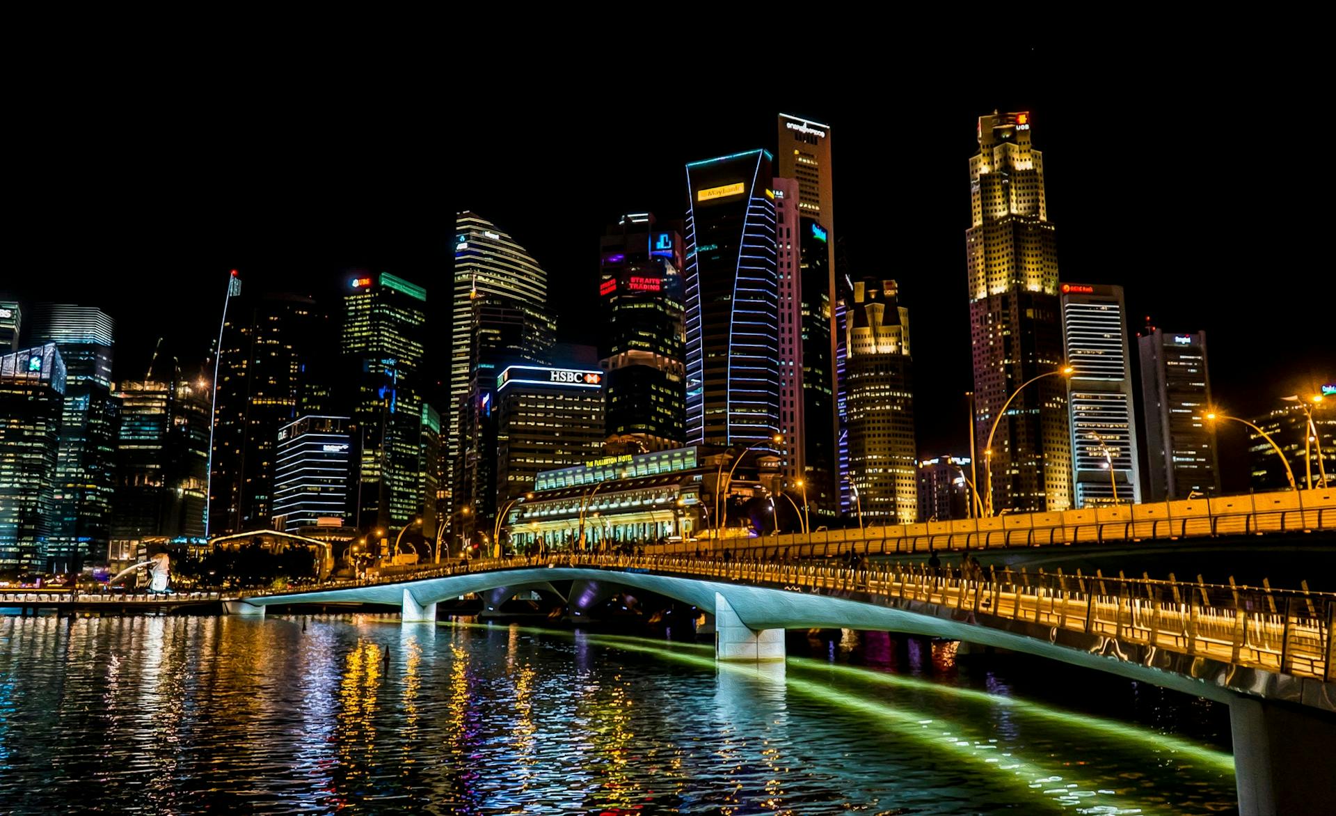 Stunning Singapore cityscape featuring vibrant skyscrapers, illuminated bridge, and reflections over the river at night.