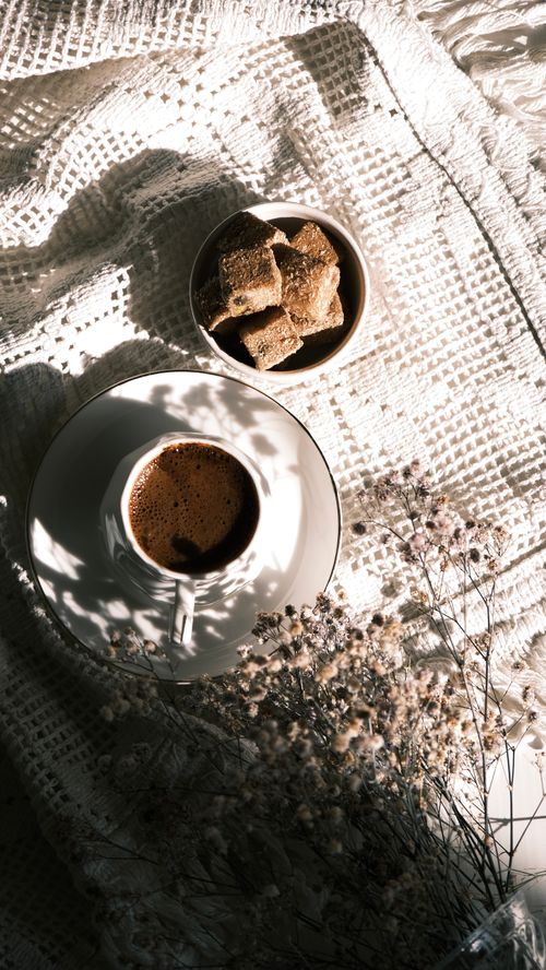 Free A coffee cup and pastries on textured cloth with soft lighting creating a serene breakfast scene. Stock Photo