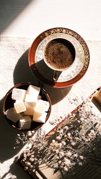 Top view of Turkish coffee with sugar cubes and an open book on a sunny table.