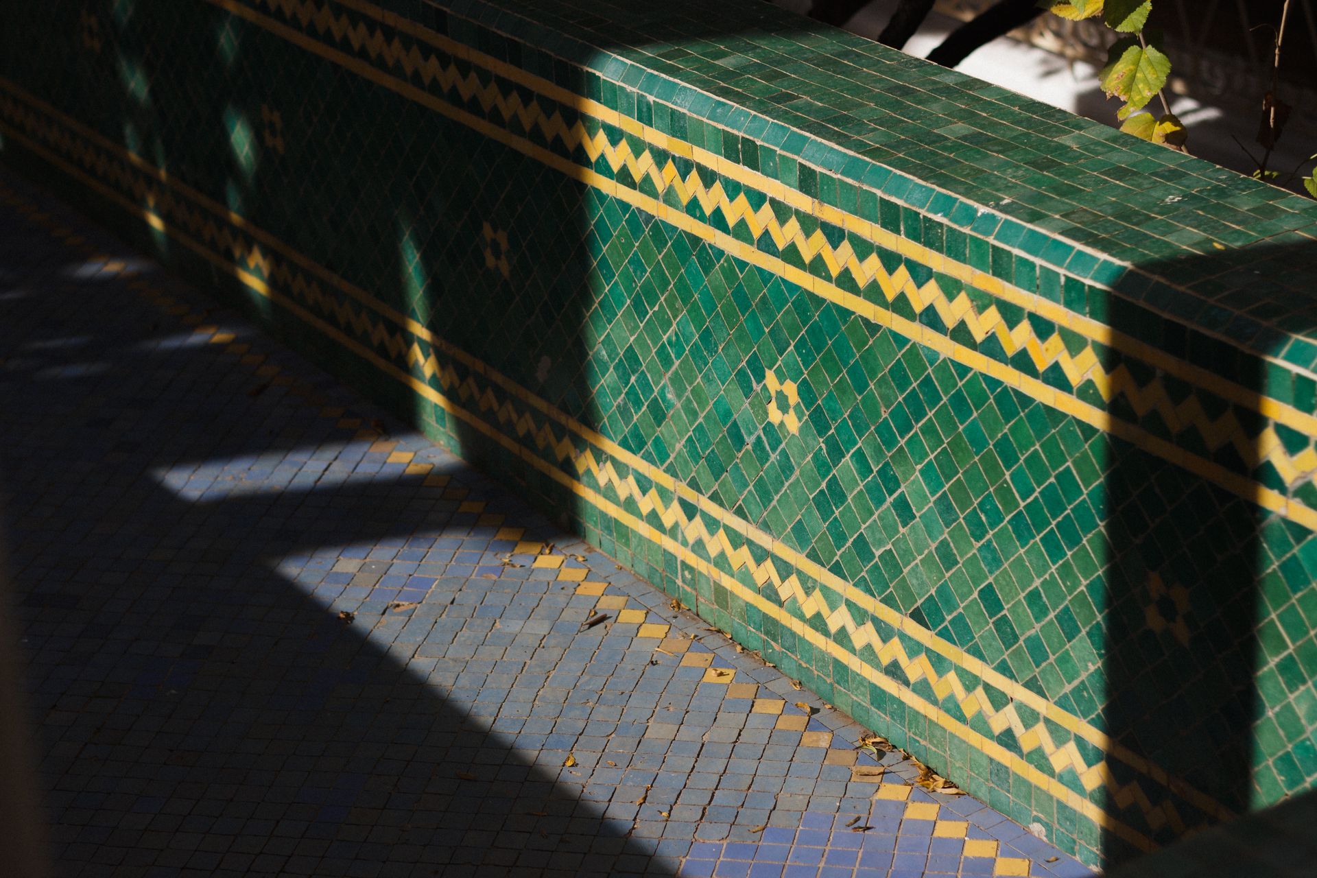 Sunlight casts shadows on a beautiful green and yellow mosaic tile wall outdoors.