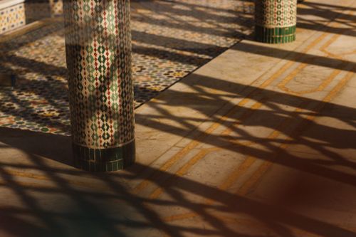Free Intricate mosaic patterns on columns casting shadows in a Moroccan architectural style. Stock Photo