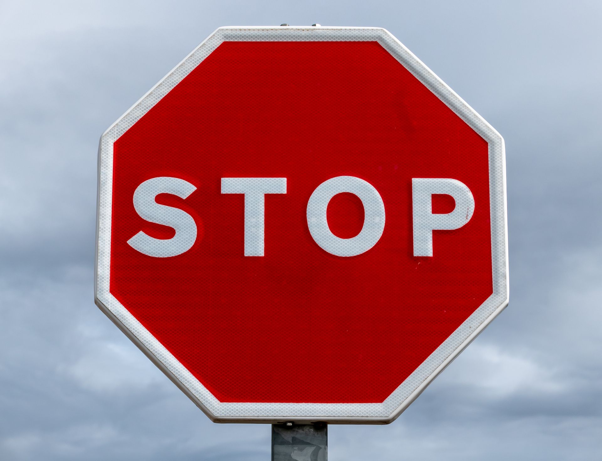 Close-up of a red stop sign with a cloudy sky backdrop, highlighting traffic regulation.