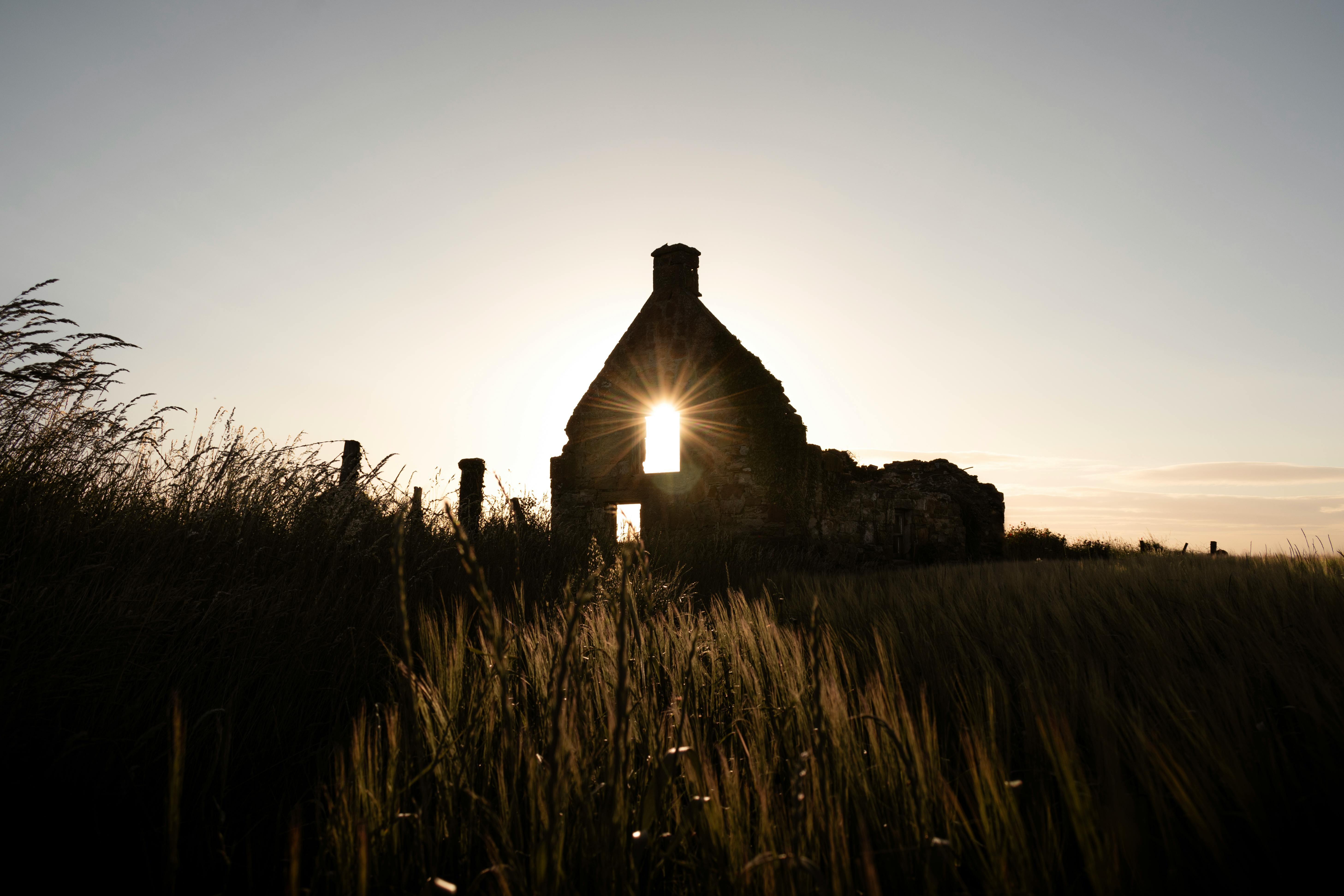 Rays of sunset through ancient ruins silhouette in grass field.