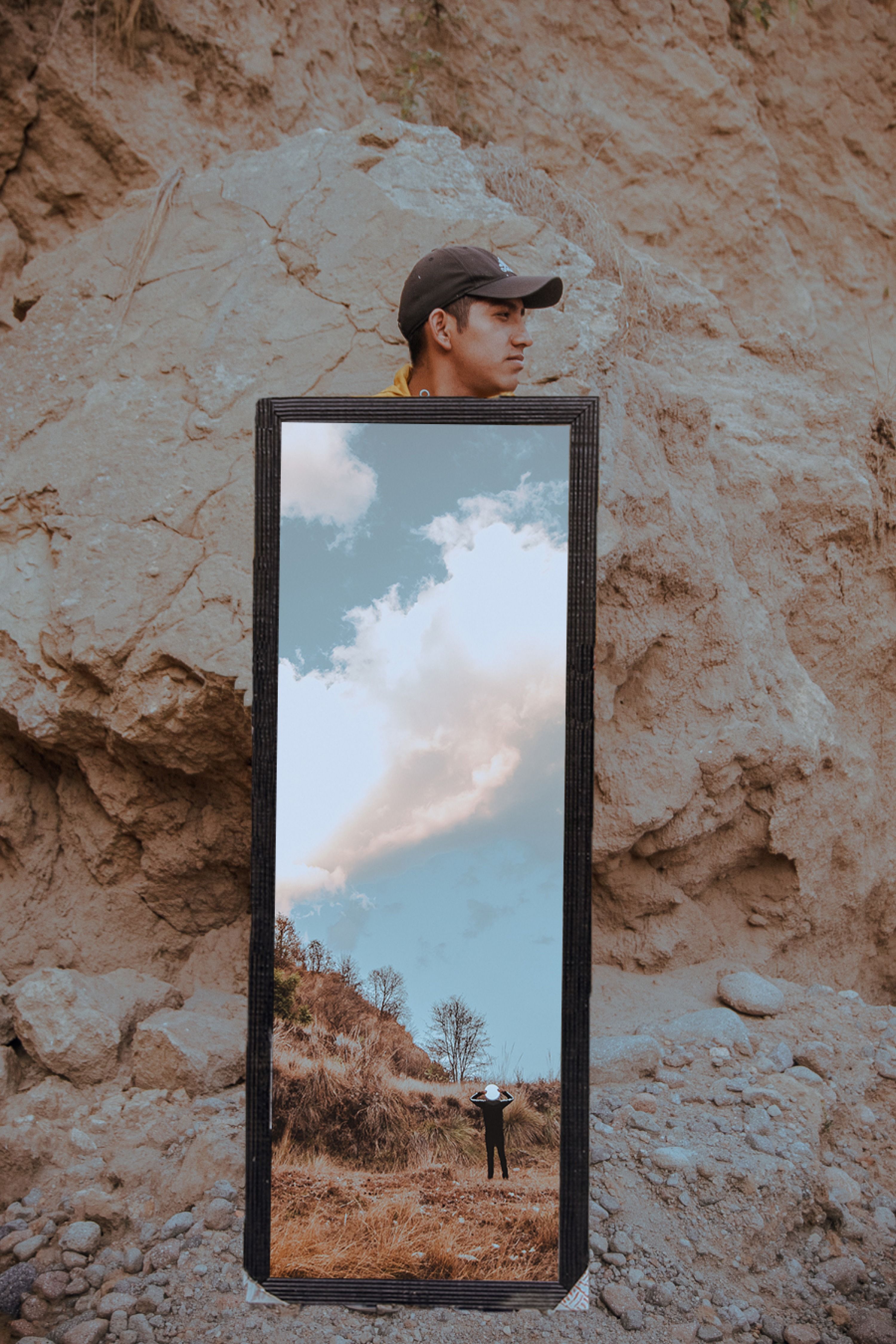 A mirror reflects a scenic sky amid a rocky terrain, adding a surreal touch.