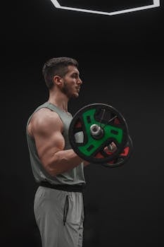Muscular man exercising with a barbell in a dimly lit gym, profile view.