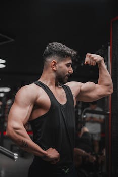 Strong male athlete flexing his bicep in a dimly lit gym, showcasing fitness and strength.
