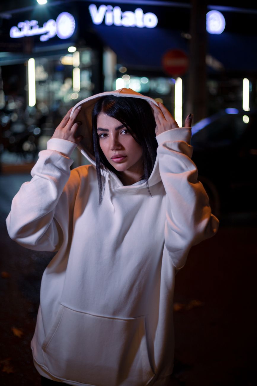 Young woman in white hoodie poses confidently on city street at night.