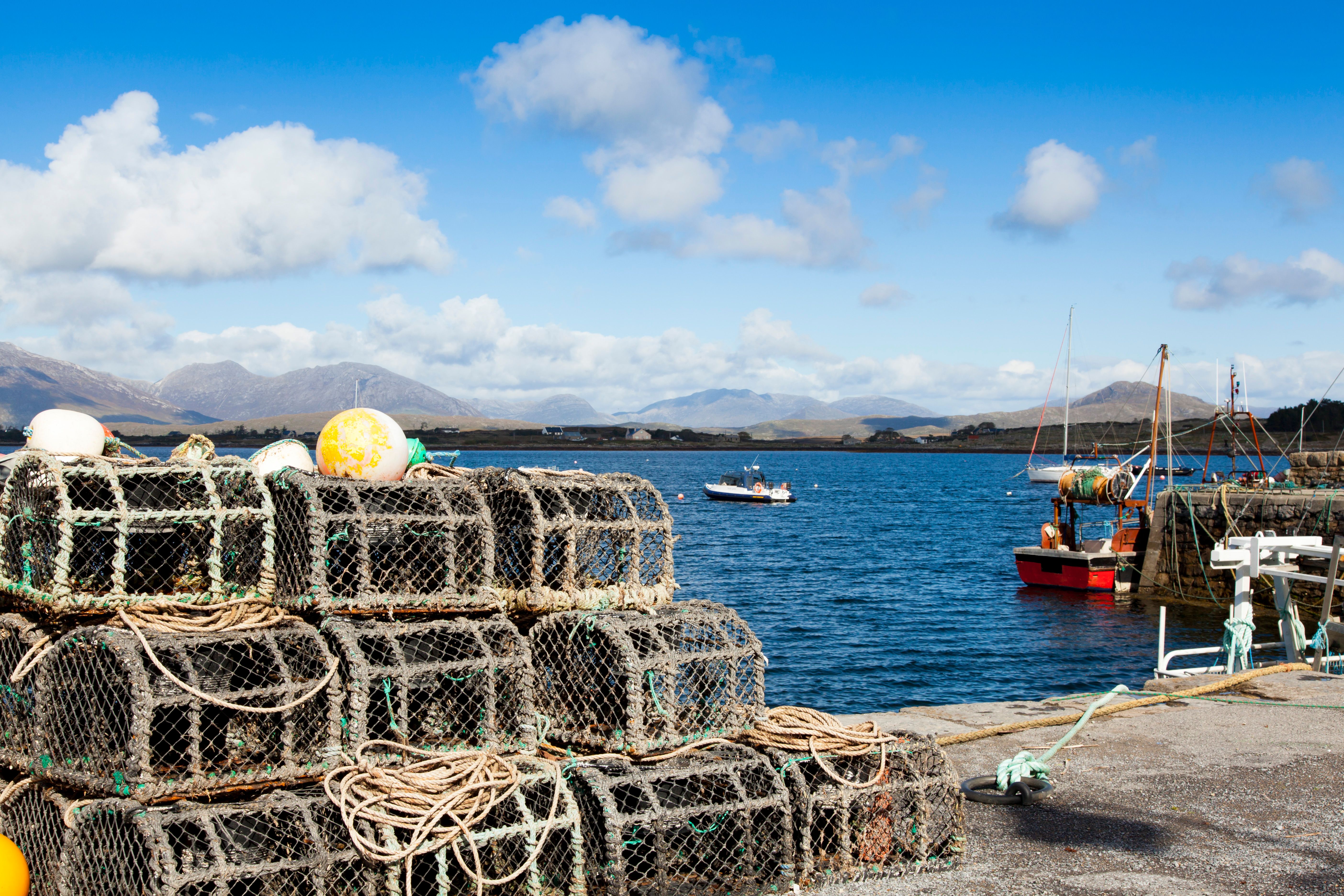 Scenic view of an Irish fishing harbor with stacked lobster pots and boats.