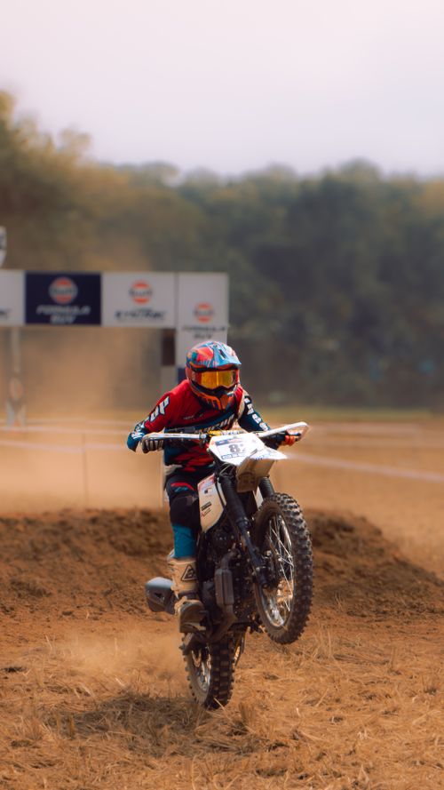Free A motocross rider in action performing a wheelie on a dirt track with dust flying. Stock Photo