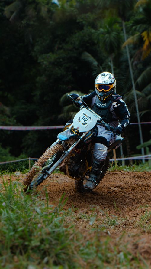 Free Motocross rider racing on a dirt track in lush surroundings, capturing speed and adrenaline. Stock Photo