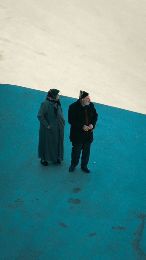 Free Elderly couple walking on a contrasting blue surface, distant view. Stock Photo