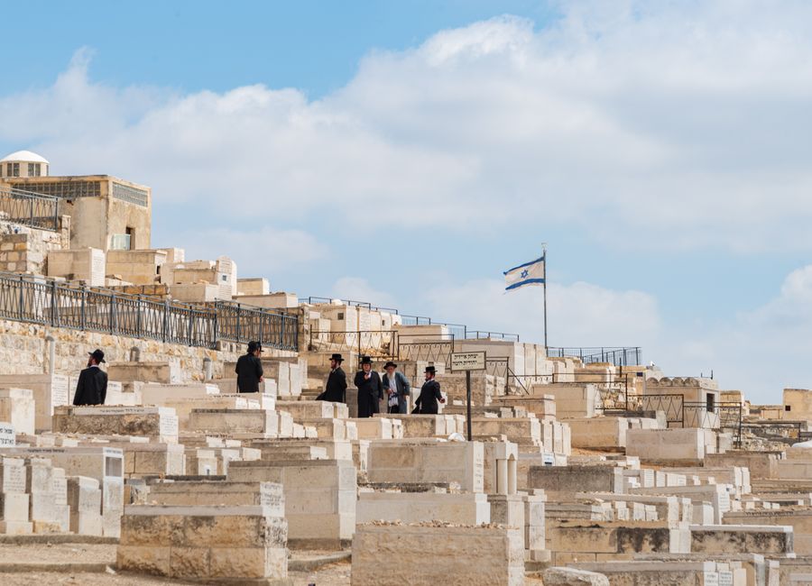 Orthodox Jewish men gather at Mount of Olives Cemetery in Jerusalem, Israel, under a clear sky.