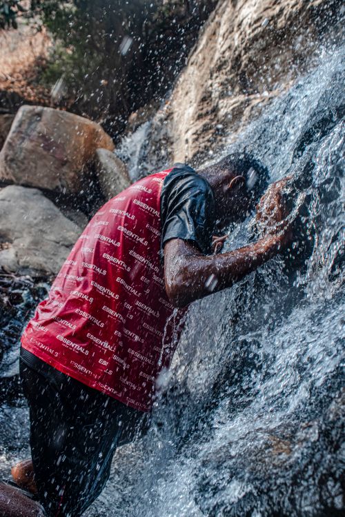 Free A man in a red shirt stands under a waterfall enjoying the refreshing water. Stock Photo