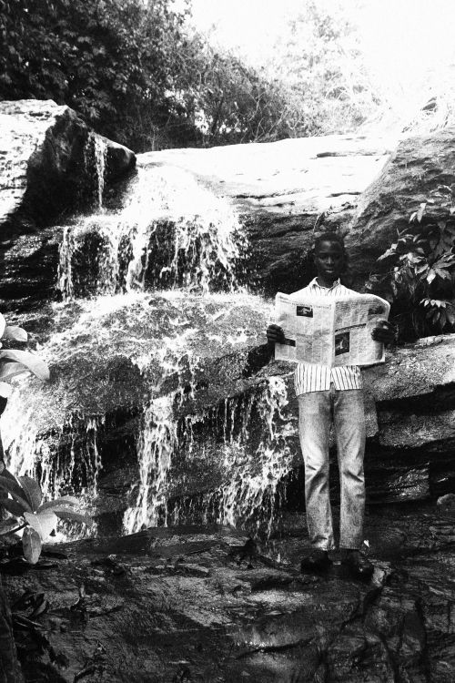 Free A man stands by a cascading waterfall, reading a newspaper. Black and white artistry. Stock Photo