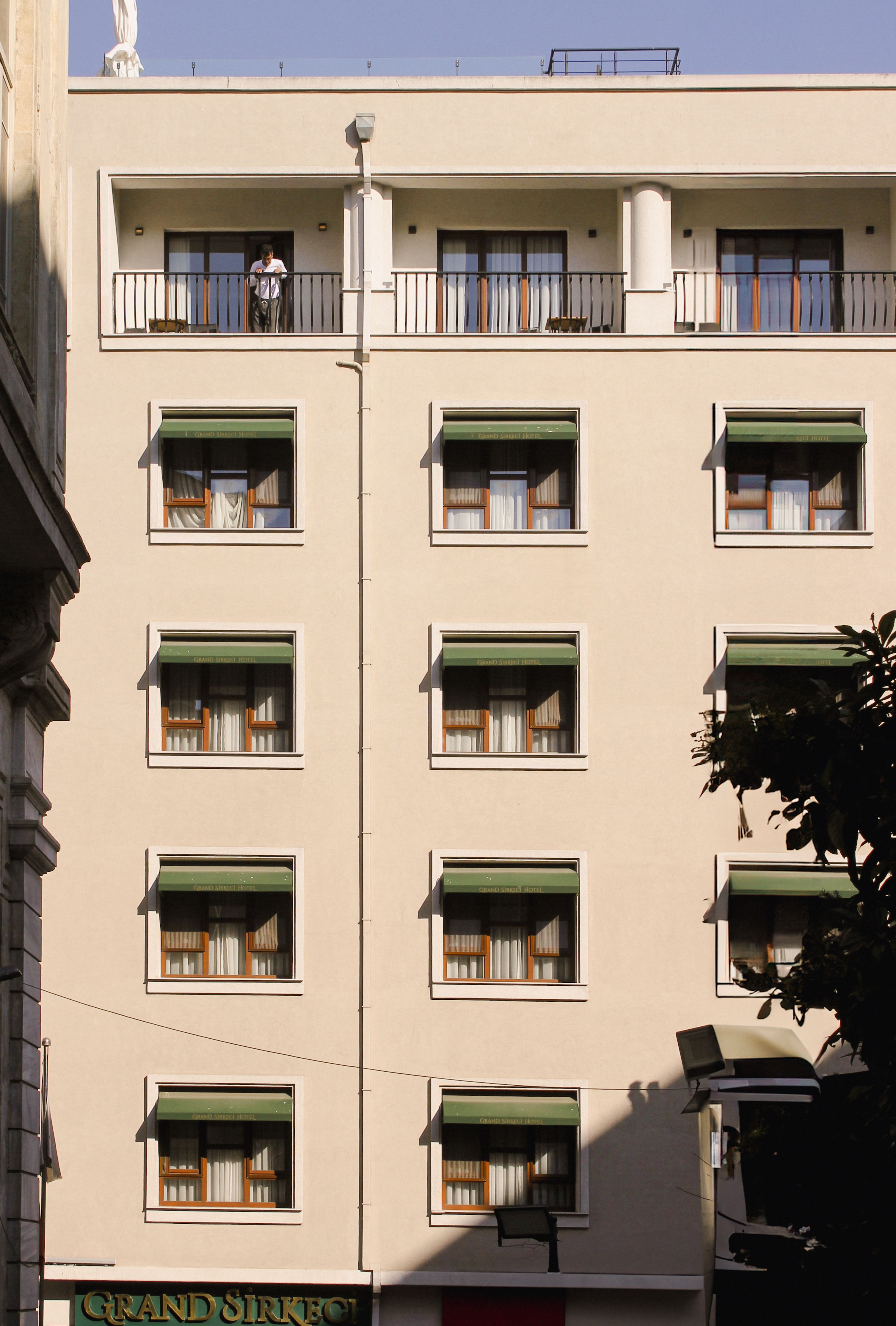 Fotomural Fachada de hotel iluminada por el sol con balcones y toldos en la ciudad.