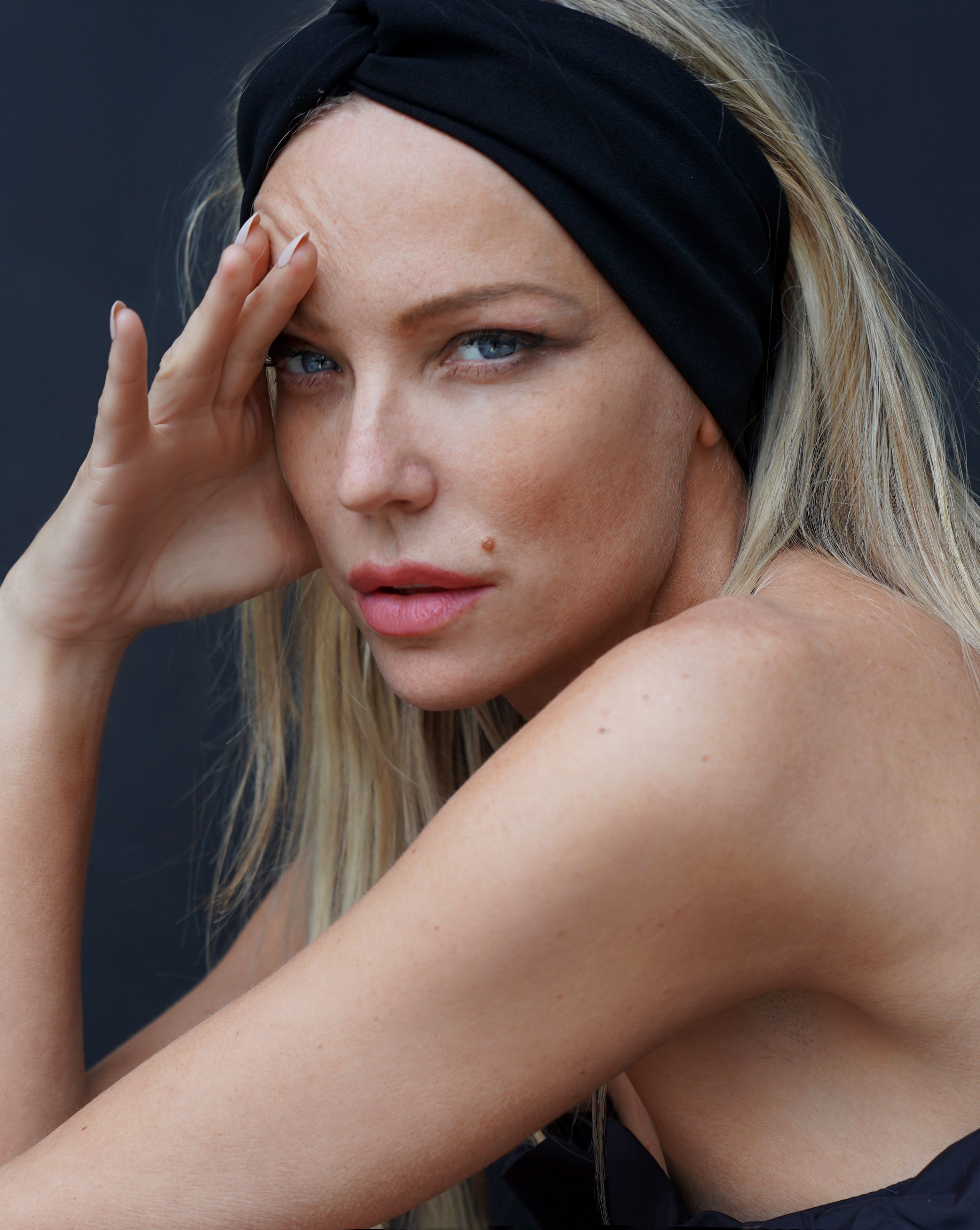 Close-up portrait of a blonde woman with a black headband, striking pose.